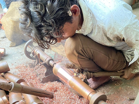 Un artesano Kaarigar da forma a una botella de cobre puro sin costuras a mano en una máquina giratoria.